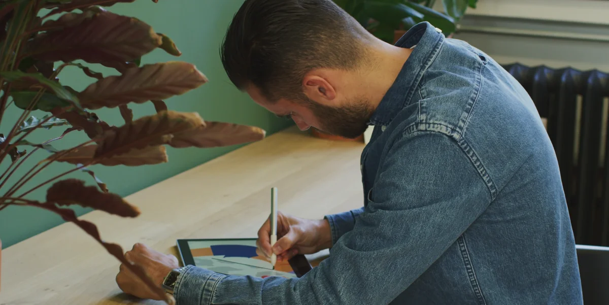 Ein Foto von einem Mann, der über einem Chromebook lehnt und mit einem Stift darauf zeichnet