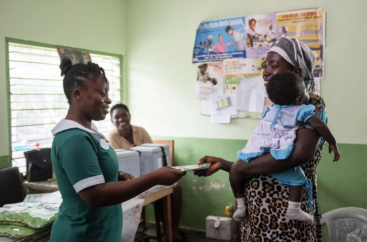 Image of a nurse handing out a piece of paper to a woman holding a baby.