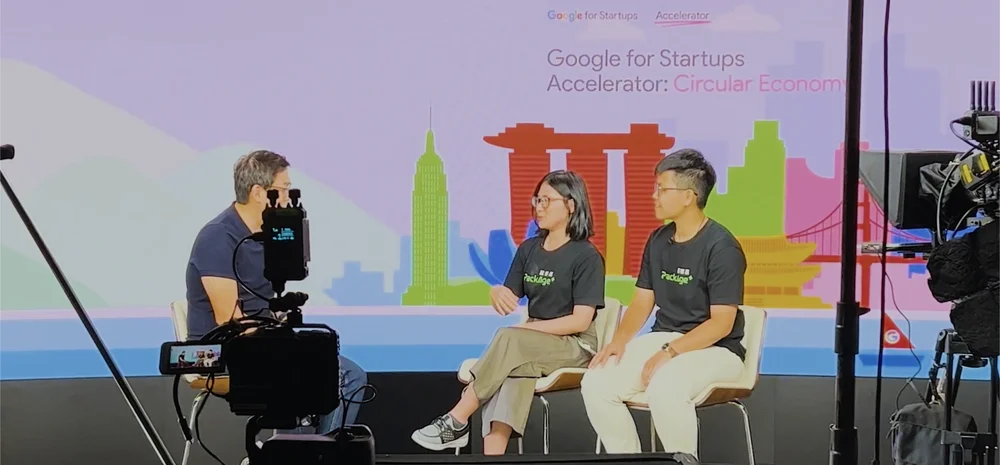 Three people sitting on stage with a camera crew recording them and the wall behind them reads: "Google for Startups Accelerator: Circular Economy"