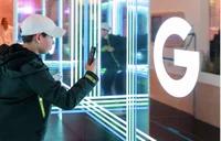 An image of a child in a cap taking a picture of a big lit up 'G' for Google