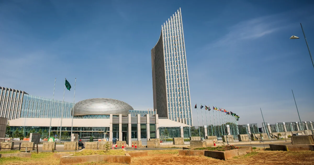 The African Union headquarters in Addis Ababa, Ethiopia, featuring a modern, high-rise tower flanked by a circular conference center and a row of flags representing member countries against a clear blue sky.