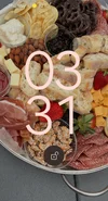 A screenshot of a Pixel lockscreen showing the time 3:13 in a pink hue and a photo of a charcuterie board in the background.