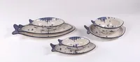 The image displays a set of three ceramic bowls and plates shaped like fish, each in varying sizes. They are characterized by a white base decorated with blue speckles against a plain white background. These pieces visually blend the iconic cobalt decorations typical of Bolesławiec pottery with elements reminiscent of Japanese porcelain.