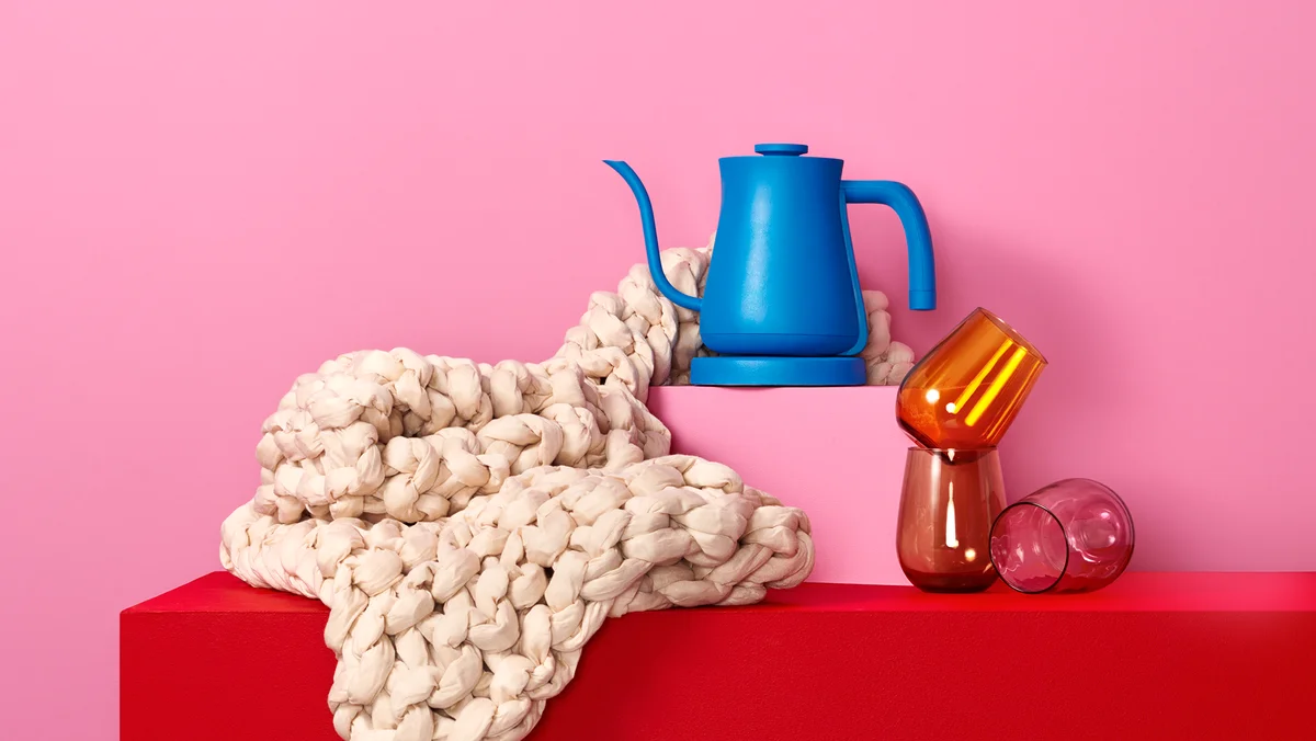 A blue kettle, a cream weighted blanket and three red wine glasses sit on top of a red table.