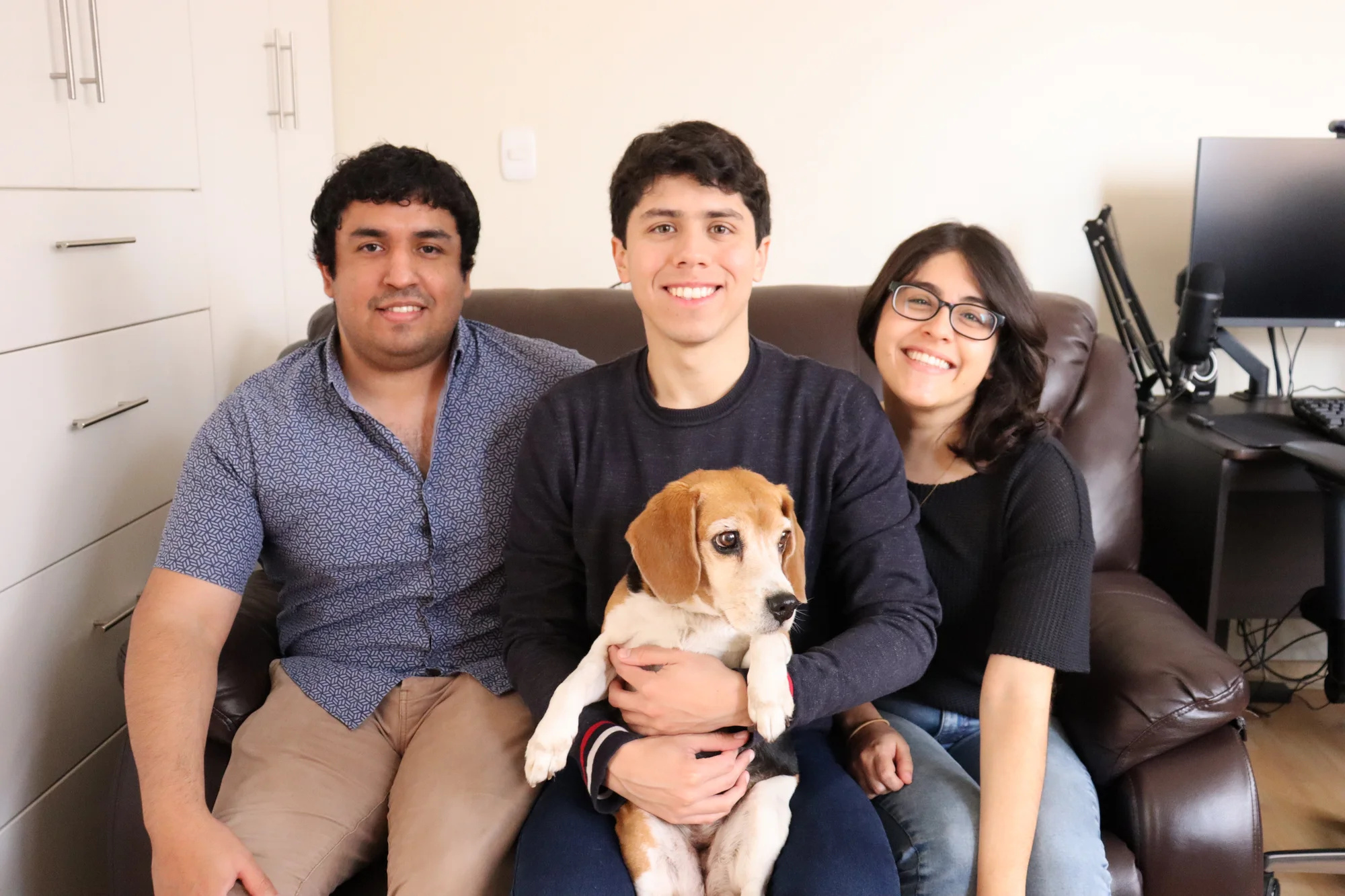 Three people sit together with a beagle in their lap.