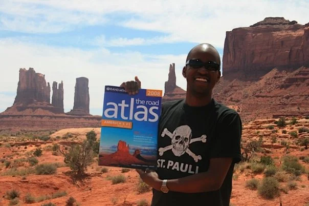 Foto von Jason vor roten Felsen in Arizona, er trägt ein St.Pauli T-Shirt und hält einen Atlas in der Hand.