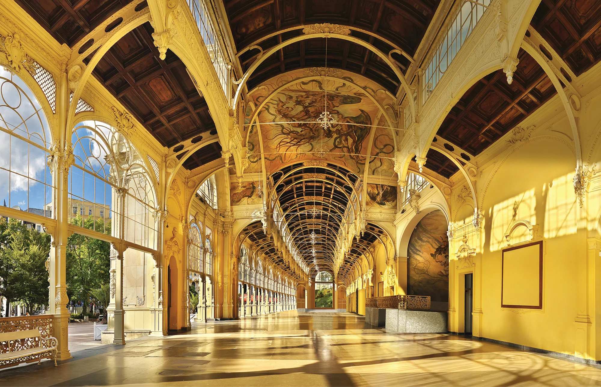 A  long hallway of golden yellow arches with seeping sunlight and decorated walls.