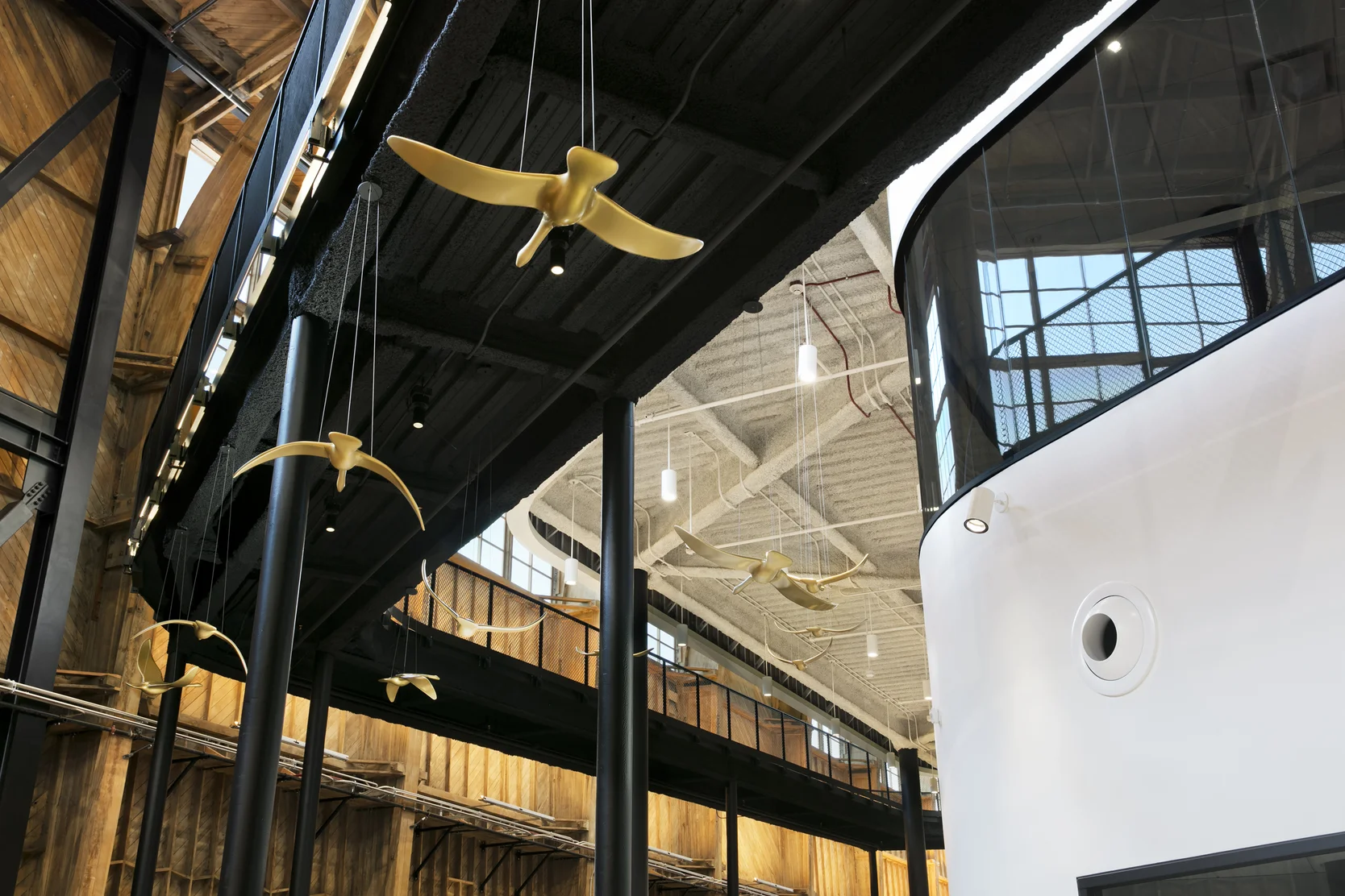 Interior image of the building shows a walkway and the exterior of a modern building. Golden gooses hang from the ceiling.