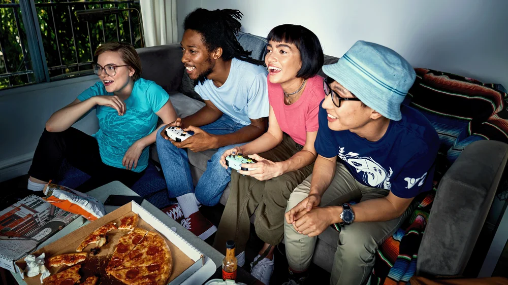 A group of friends gather on the couch while playing a Stadia game on their TV.