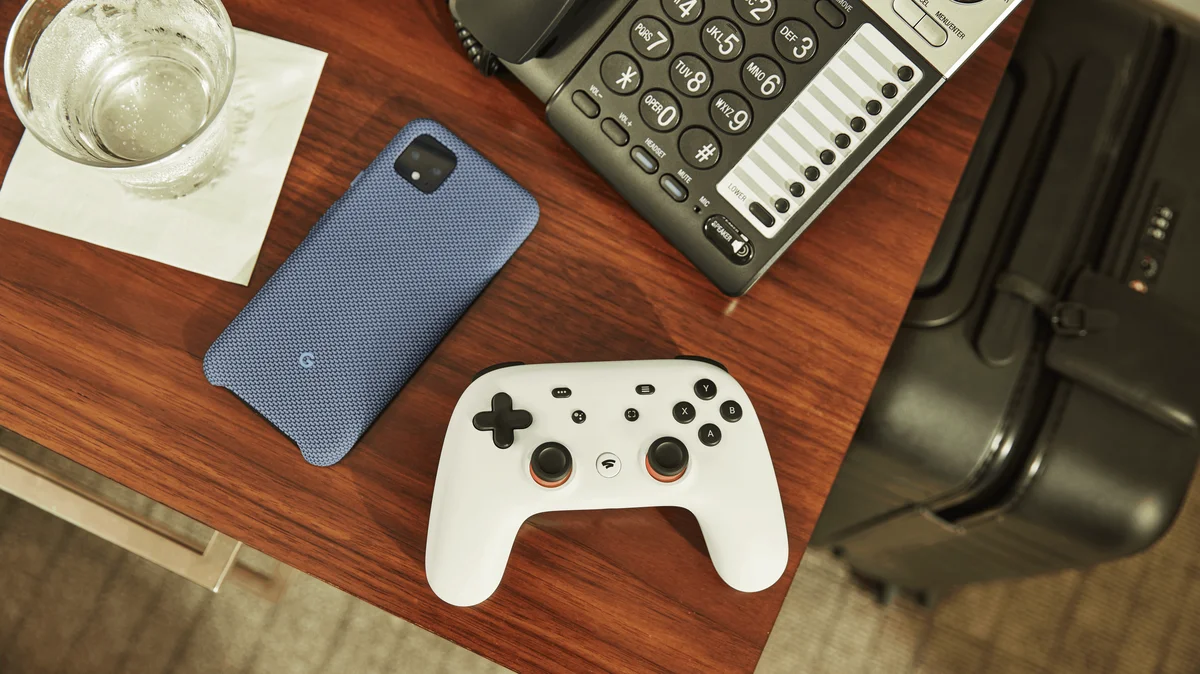 A top down perspective of an office desk shows a blue Google Pixel phone and a white Stadia Controller.