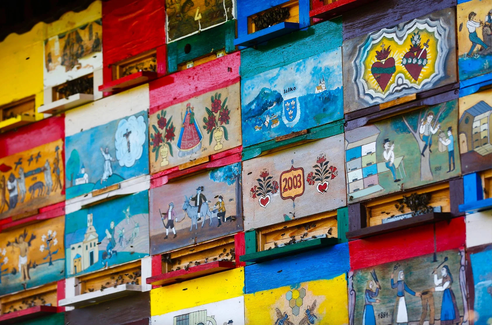 A wall of beehive panels, all of which have been painted brightly with different illustrations of people, landscapes and symbols like hearts