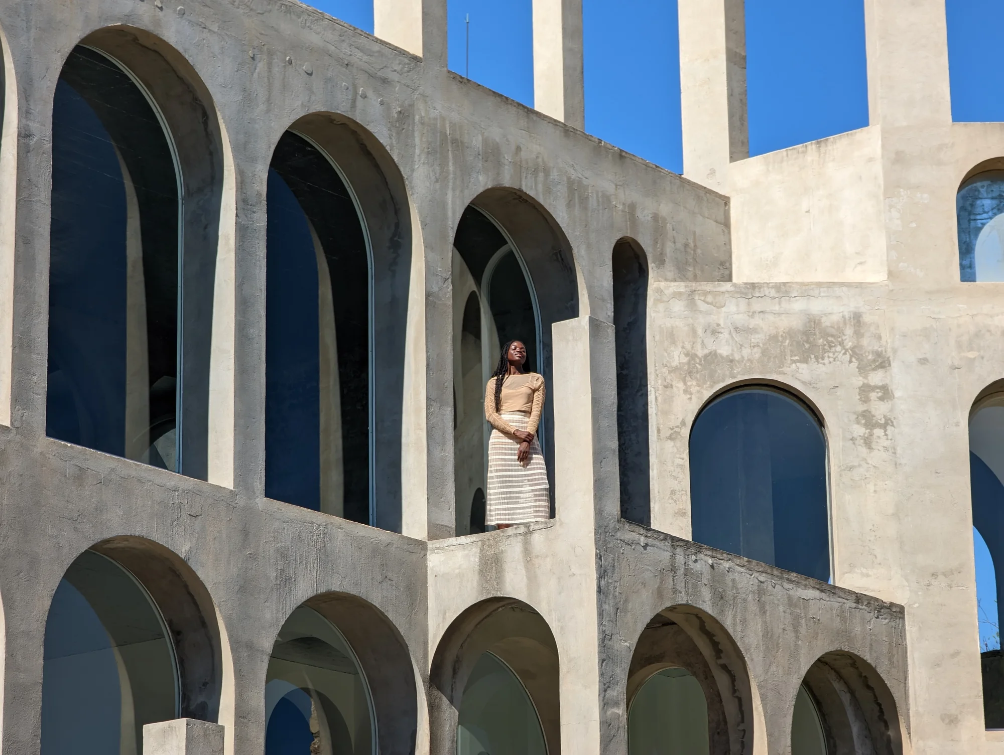 A carousel of four photos. The third shows the same image, zoomed in even more to focus on the third level of the building, revealing a woman standing in between two columns.