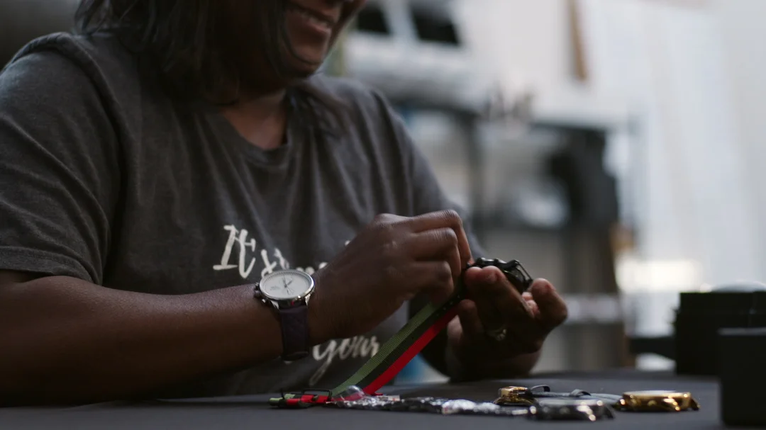 A woman works on a watch with a green, black, and red striped watch band