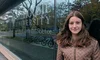 Image shows a young woman with brown hair wearing a brown coat, looking into the camera and smiling. She's standing against a window to a building that says "Dalhousie University, department of Computer Science."