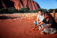 A Maruku Artist teaching another person about traditional symbols by drawing in the sand, on Anangu Country