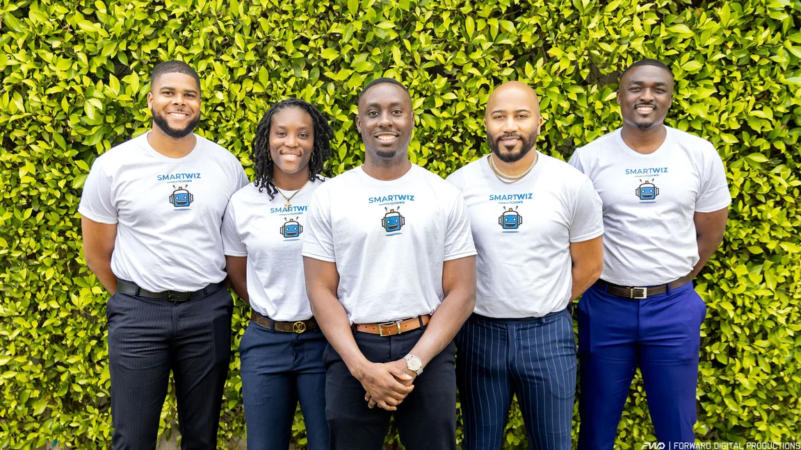 Five people wearing white "Smart Wiz" shirts and dark pants stand side-by-side in front of a green living wall.