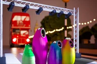 4 colorful blobs on stage with a red bus from in the background