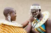 An image of two Maasai women with shaved heads wearing beaded necklaces, earrings and a beaded headband