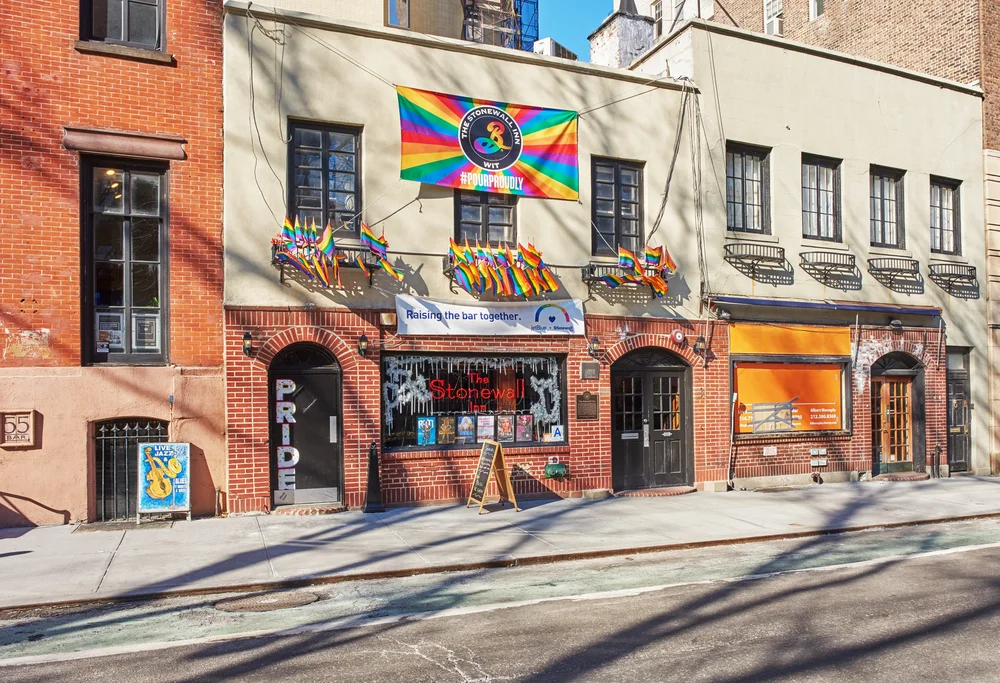 Exterior photograph of the Stonewall Inn bar in New York City with rainbow Pride flags visible.