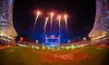 A packed baseball stadium illuminated by a dazzling fireworks display during the Tomateros Festival. The vibrant colors of the fireworks light up the night sky above the cheering crowd, creating a festive atmosphere.