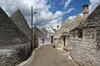 A group of conical shaped gray roofs with white brick walls on two sides of a small street.