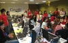 Three rows of people sitting and standing at desks with laptops and monitors inside an office with a Google sign on the wall.