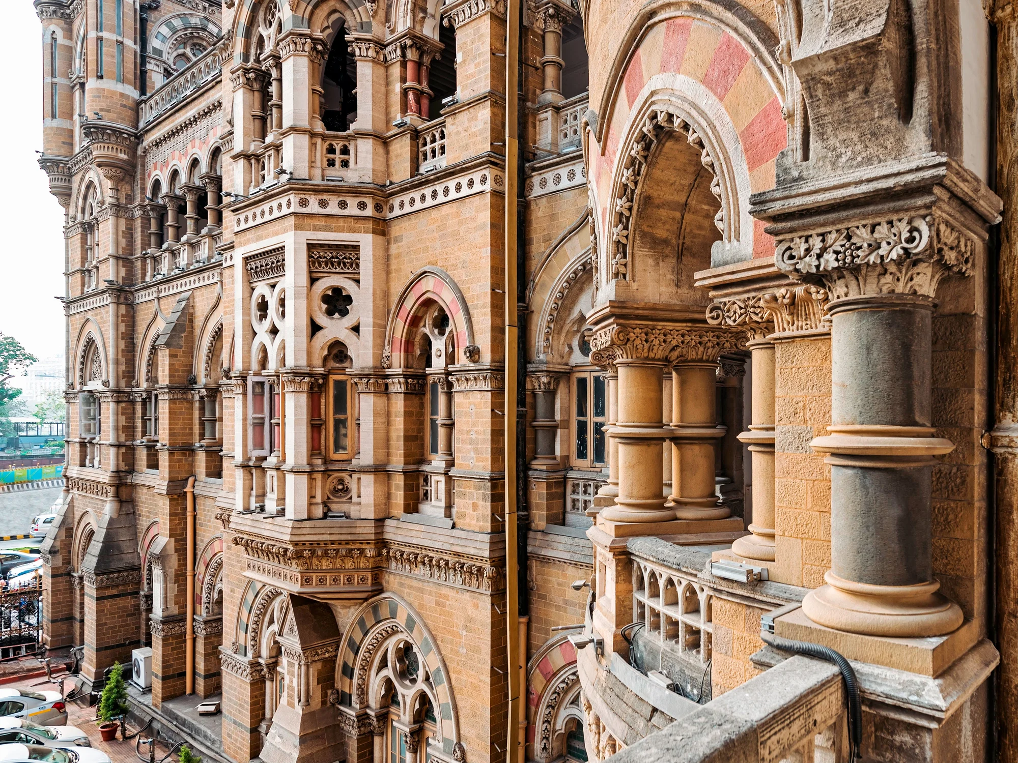 Color photograph of an intricate exterior of a tan, white, grey building with archways, pillars, and ornate carvings.