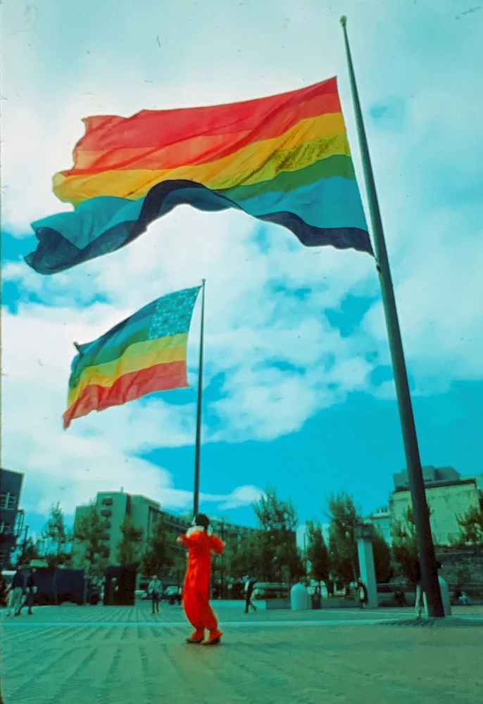 A person dressed in red standing under 2 colorful flags that flow in the wind