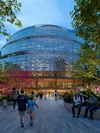 A rendering of a large, modern glass building - the redesigned Thompson Center -  at dusk, with people enjoying the pedestrian plaza in the foreground.