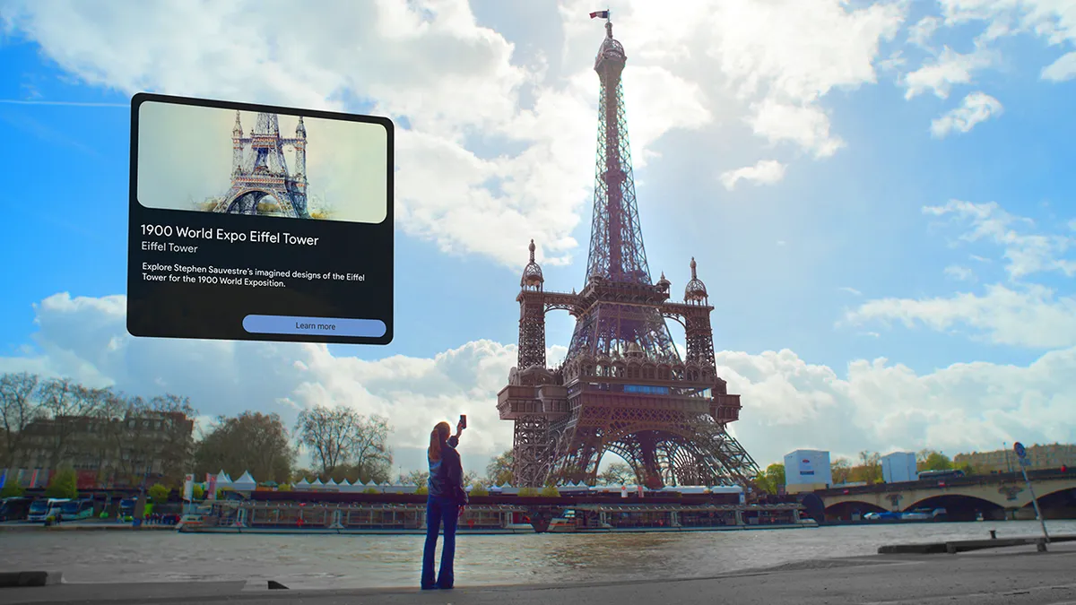 A woman is standing in front of the Eiffel Tower with a phone. Extra structure is built onto the Eiffel Tower and a copy box is on the left hand side.