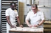 Two bakers, one young, one middle aged, at work together shaping dough