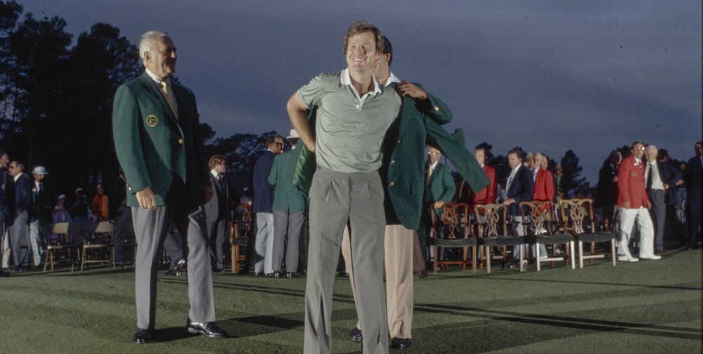 Golfer Tom Watson receiving a green jacket at a major competition with a crowd gathered behind.