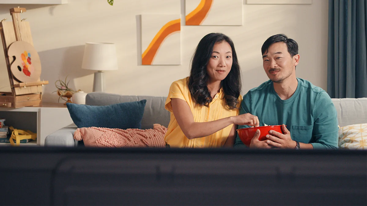 Two people sitting on a couch and sharing a bowl of popcorn while watching TV.