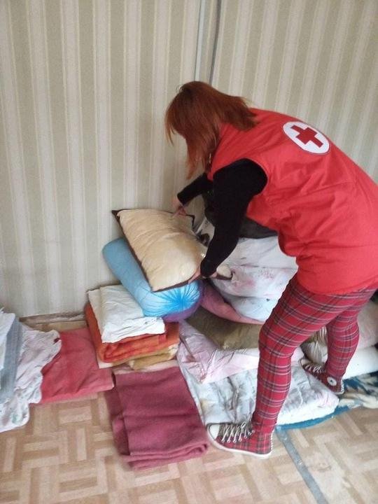 A woman in a Red Cross uniform puts bedding in a pile on the floor