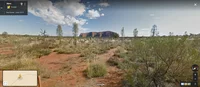 Street View imagery of Uluṟu-Kata Tjuṯa National Park, with a view of Uluru in the background and the desert landscape and foliage in the foreground