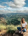 A person sitting at the top of a hike looking into the camera, smiling.