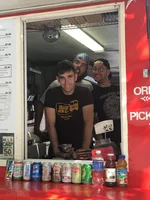 Three people stand at the window of a food cart, all looking out toward the camera.