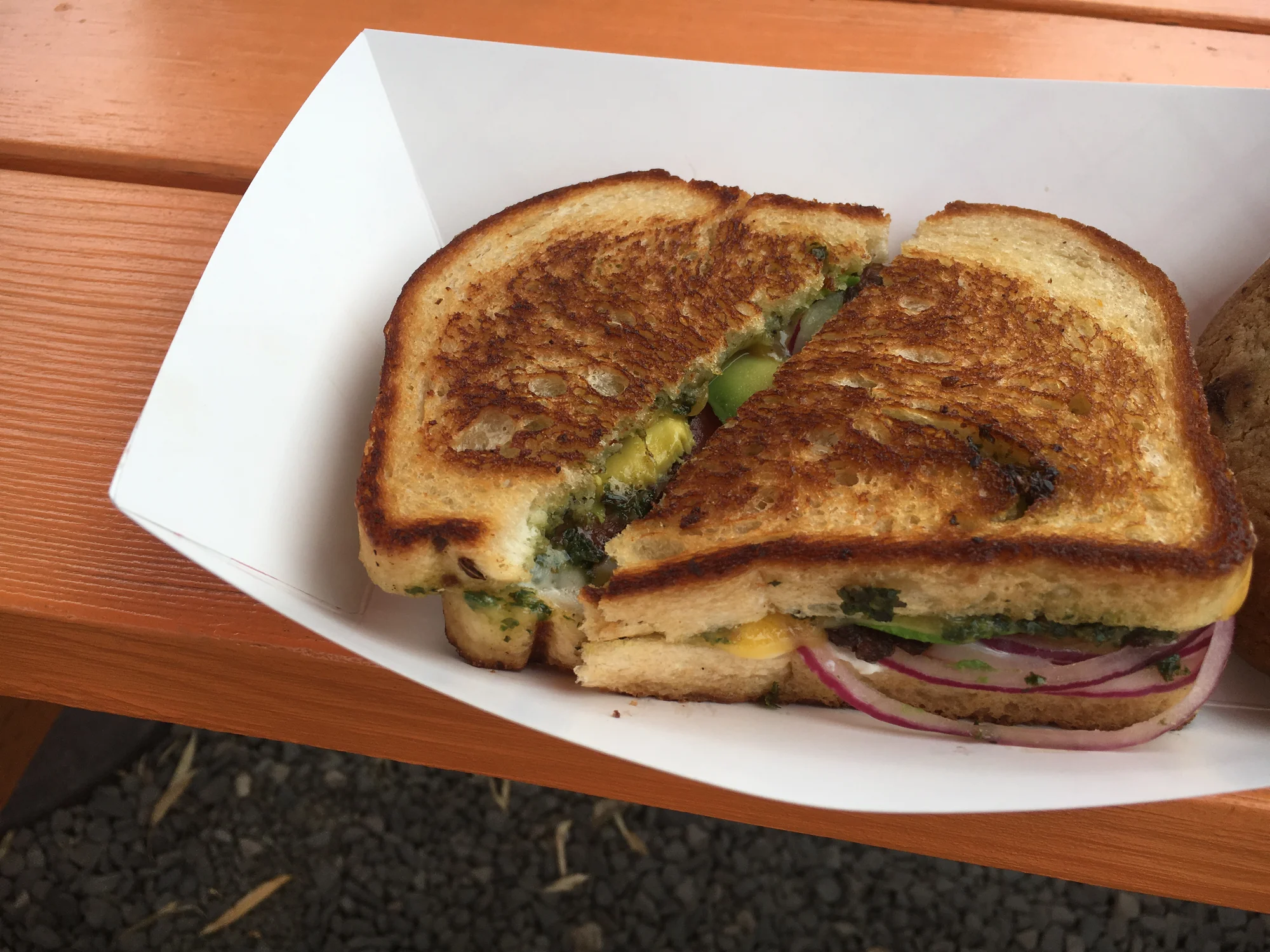 A grilled cheese sandwich with onions in a paper to-go bowl.