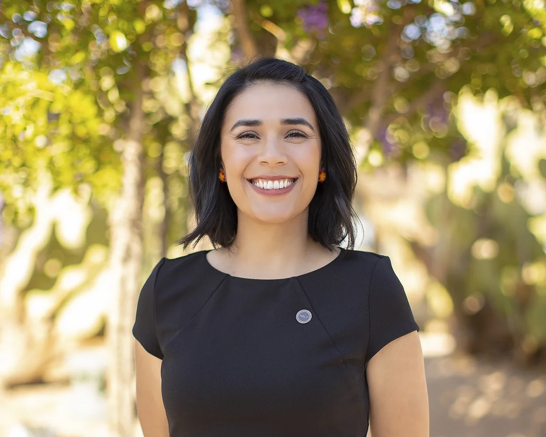 Photograph of Juliana Urtubey in a black shirt with a green botanical background