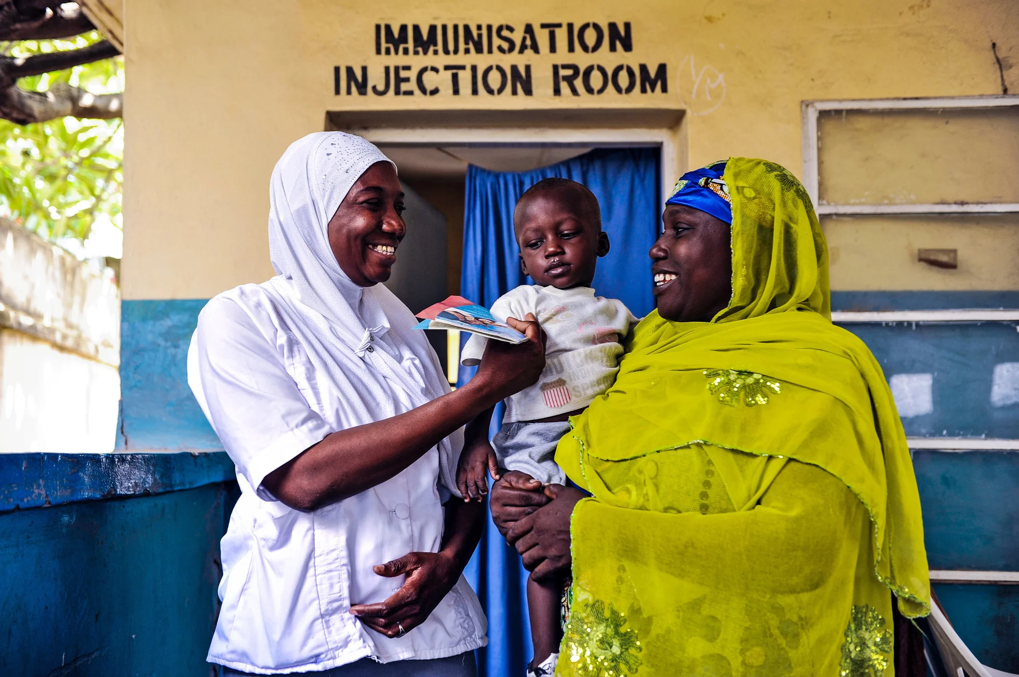 A photograph of two women talking outside a vaccination room holding a child