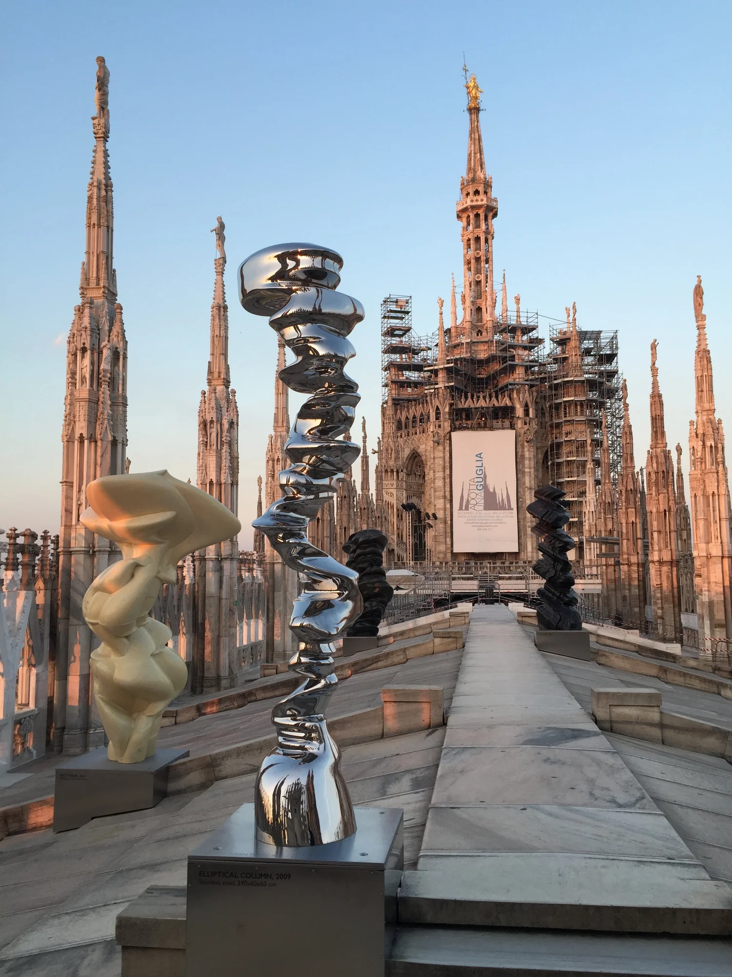 On the terrace of the Cathedral rooftop, at sunset, a  contemporary art exhibit contrasts with the ancient Gothic spires.