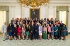 A large group of people — the 2022 State Teachers of the Year, President Joe Biden and First Lady Dr. Jill Biden, and Secretary of Education Miguel Cardona  — pose in front of a portrait of Abraham Lincoln. Above them is a golden chandelier.