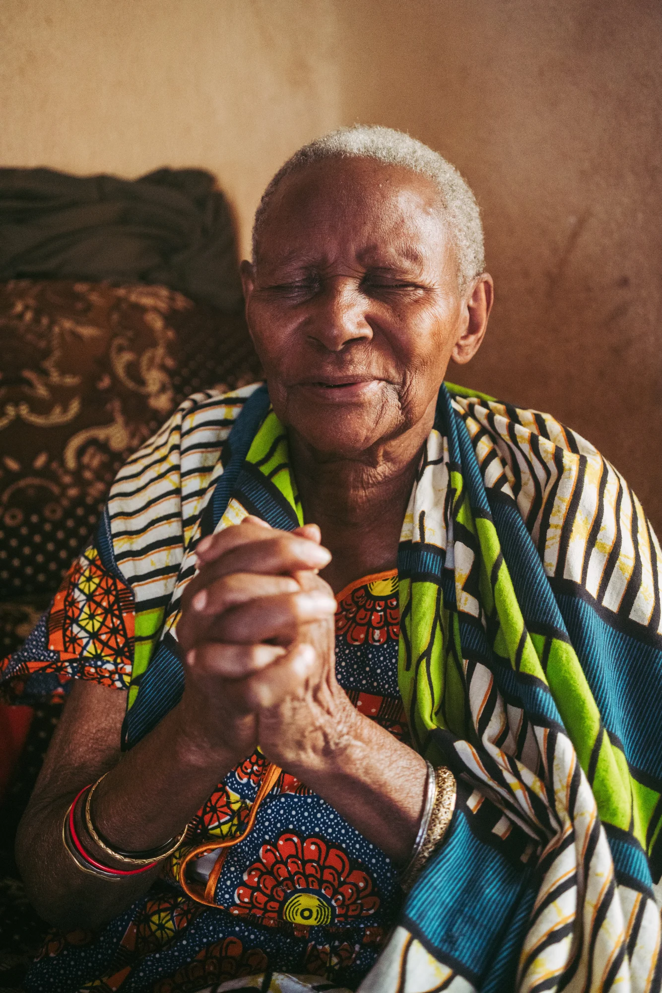 A woman from Shimbwe, in colorful local clothing, with eyes closed and hands clasped.