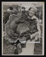 Old, black and white photograph of a smiling woman holding a giant cabbage