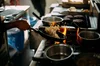 Several cooking pots on a stove, with vegetable fried rice being cooked with yak meat