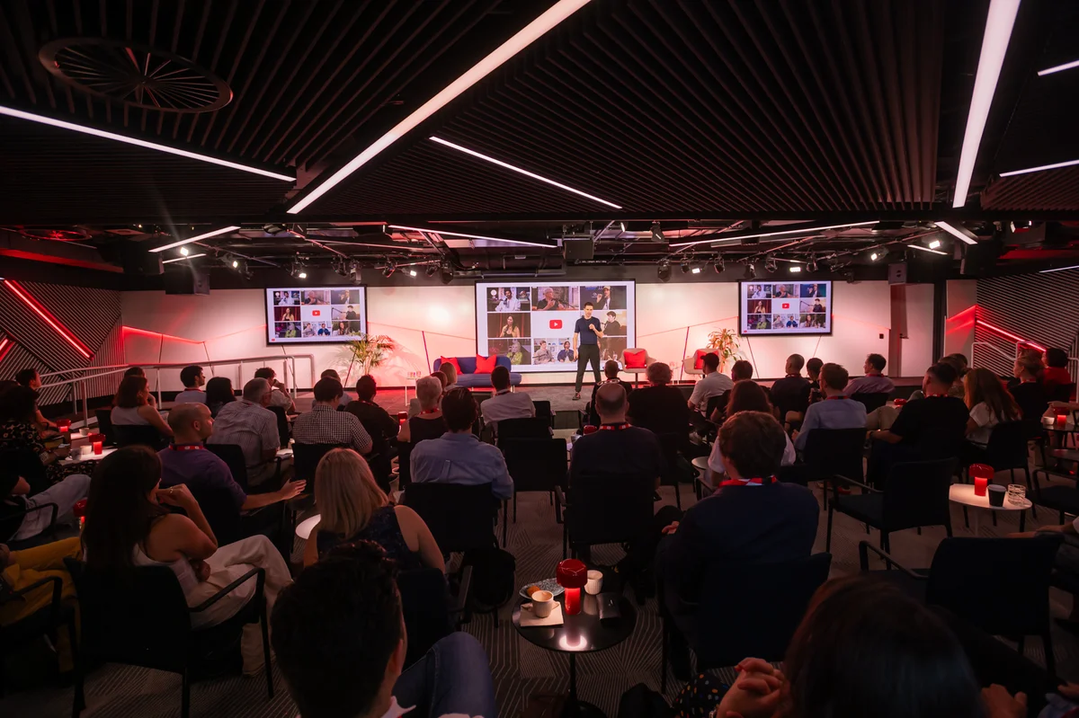 A man stands on a small stage presenting to a room full of people