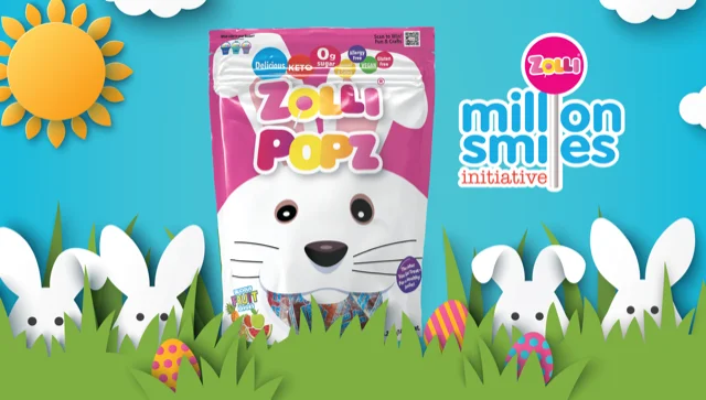 A bag of Zolli Popz candy sits in the middle of an illustration of white rabbits and Easter eggs hiding among green grass. There is a million smiles initiative  logo on the right. In the background are white clouds on a blue sky and a yellow sun.