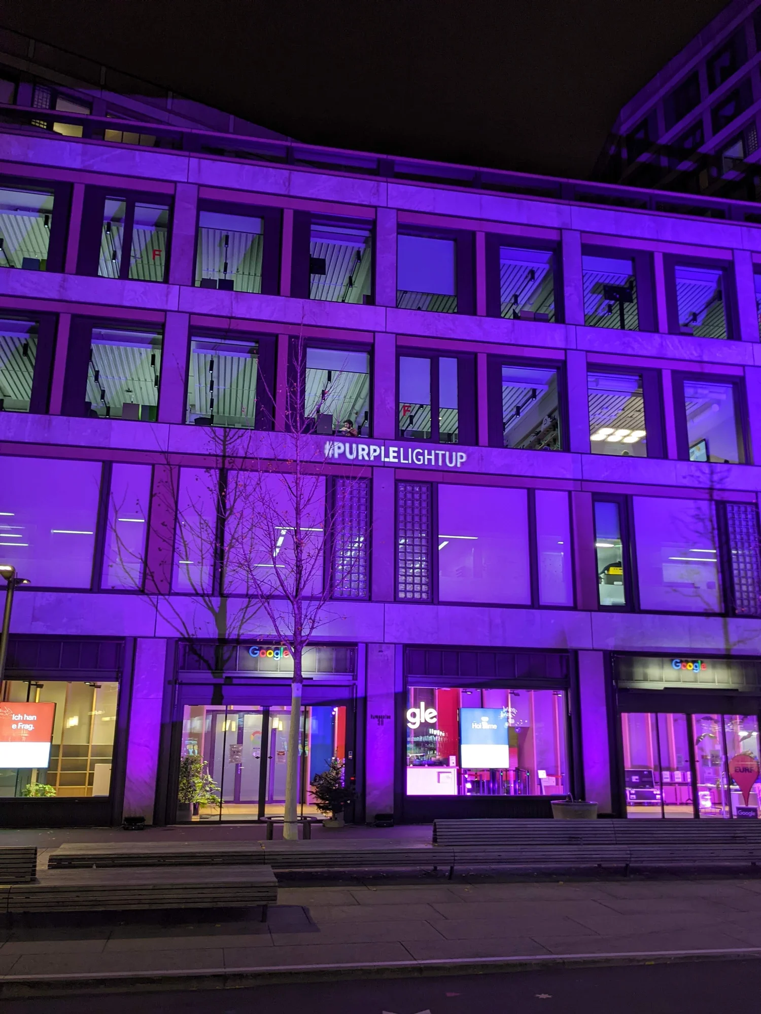 Gebäudefront des Google-Büros in der Europaallee in Zürich, welche lila erleuchtet ist. Im zweiten Stock steht ein weißer Text: #PurpleLightUp