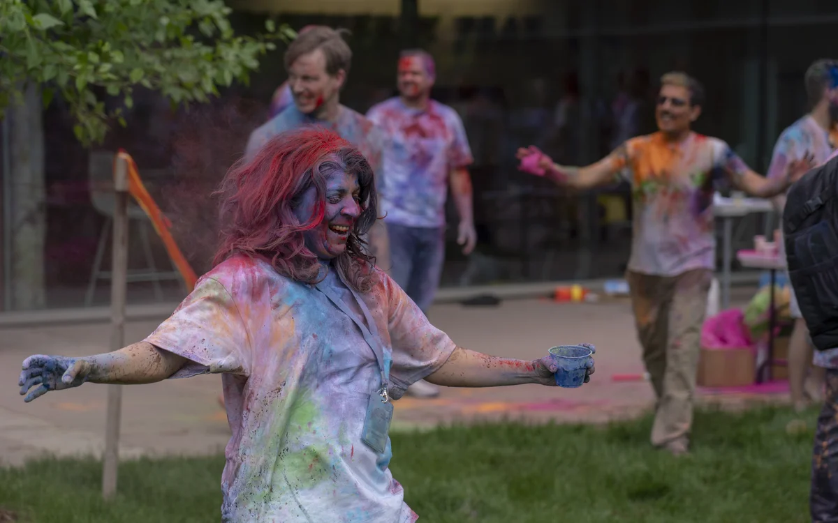 Photo of Bhavna smiling at a Holi celebration; she is covered in different colored powders, and people around her are as well.