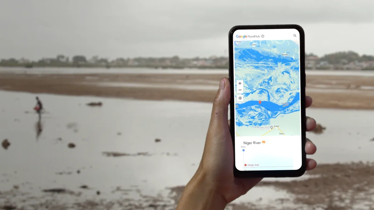 A hand holding a phone displaying Google's Flood Hub platform